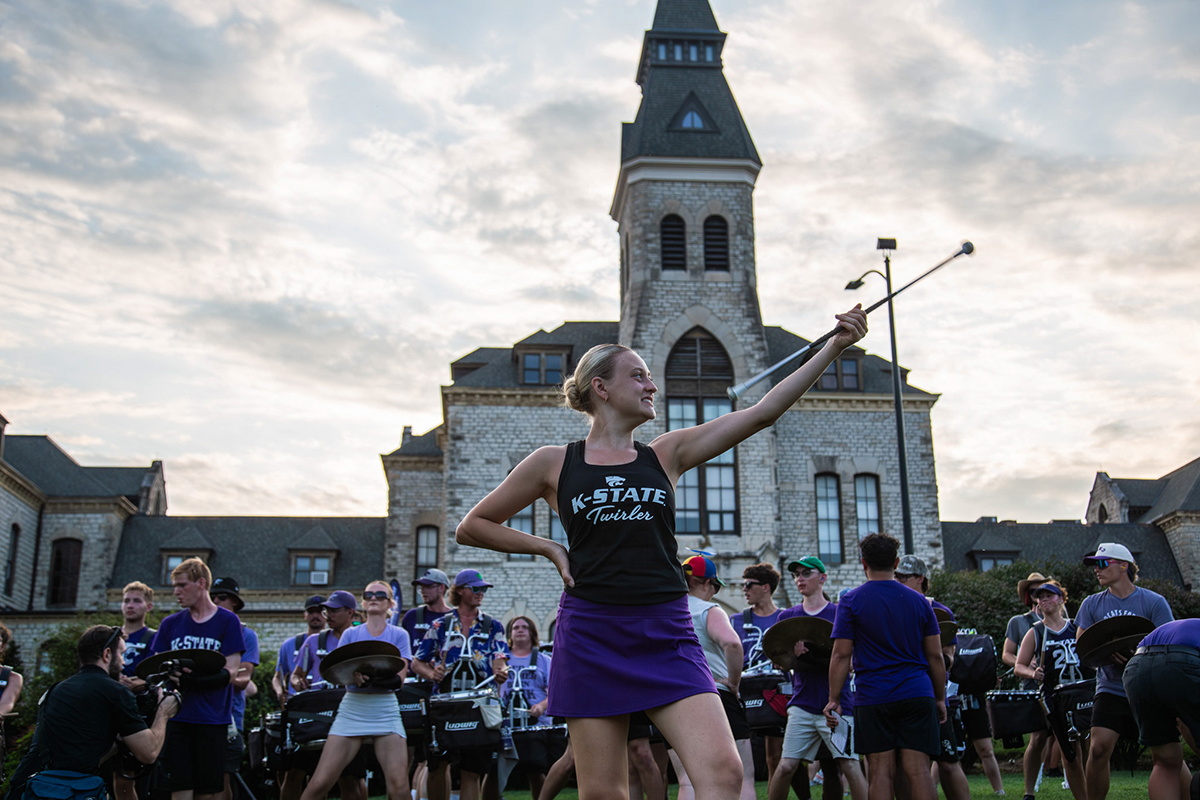 Kaylee twirling a burton while looking over sholder at the K-State band behind her back. 