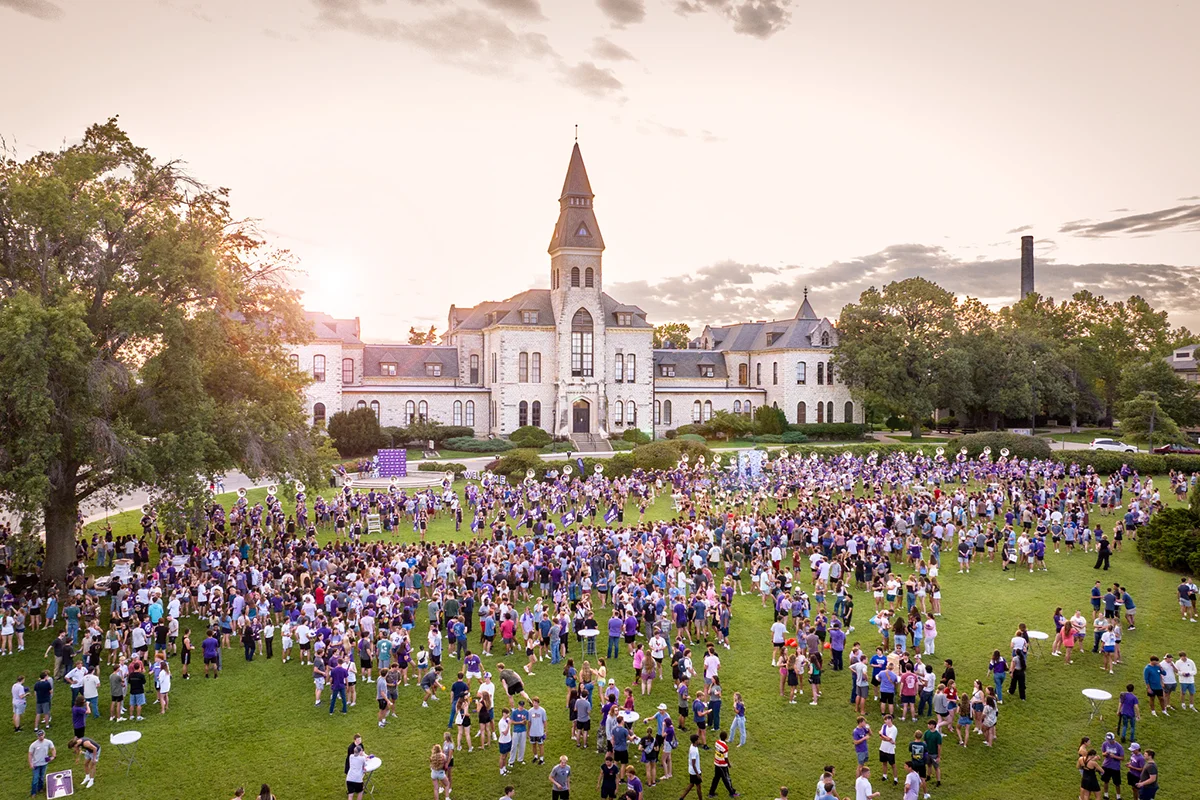 A lawn outside of university buildings filled with students and K-State bands. 
