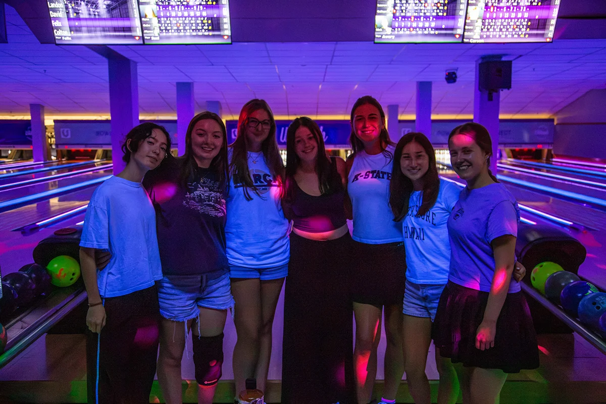A group of students pose in a neon bowling ally.