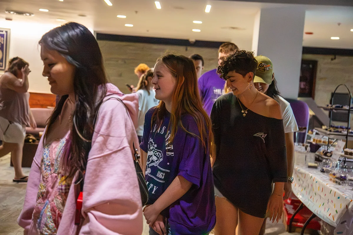 A group of students walking in a circle with cakes on the table behind them.