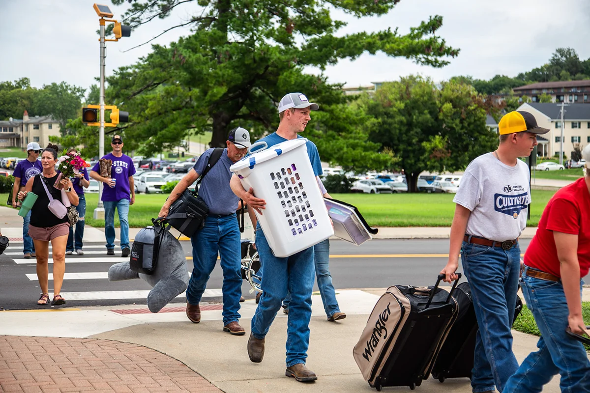 A group of families walking across a street while carrying personal items.