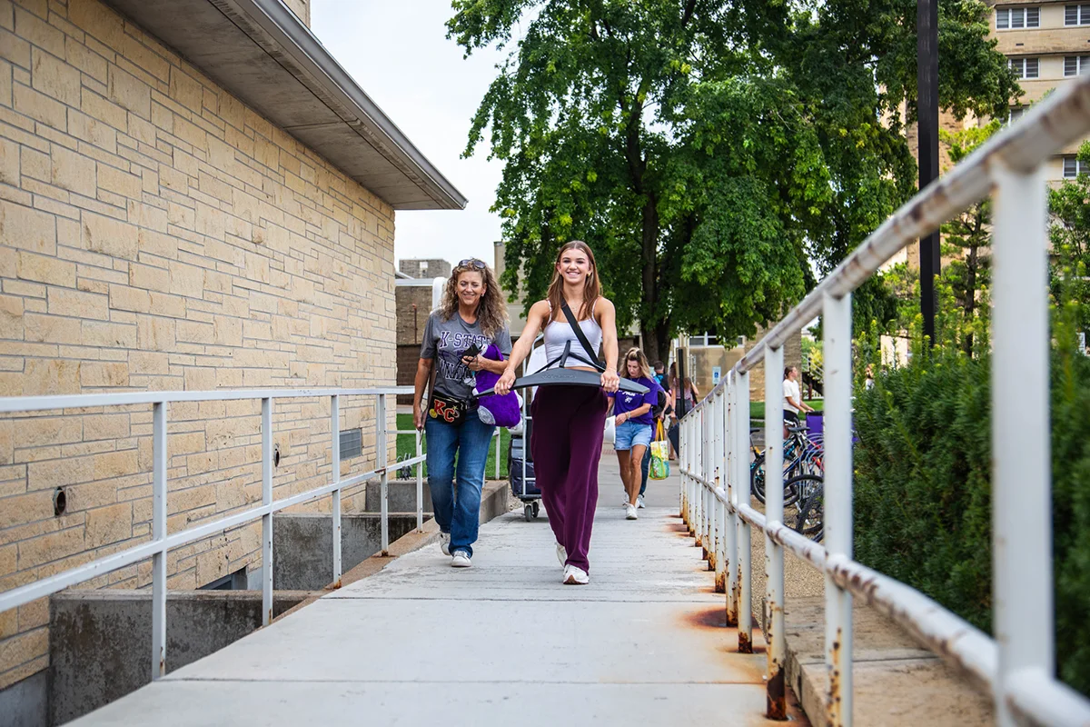 A mother and daughter walking up a ramp with dorm items.