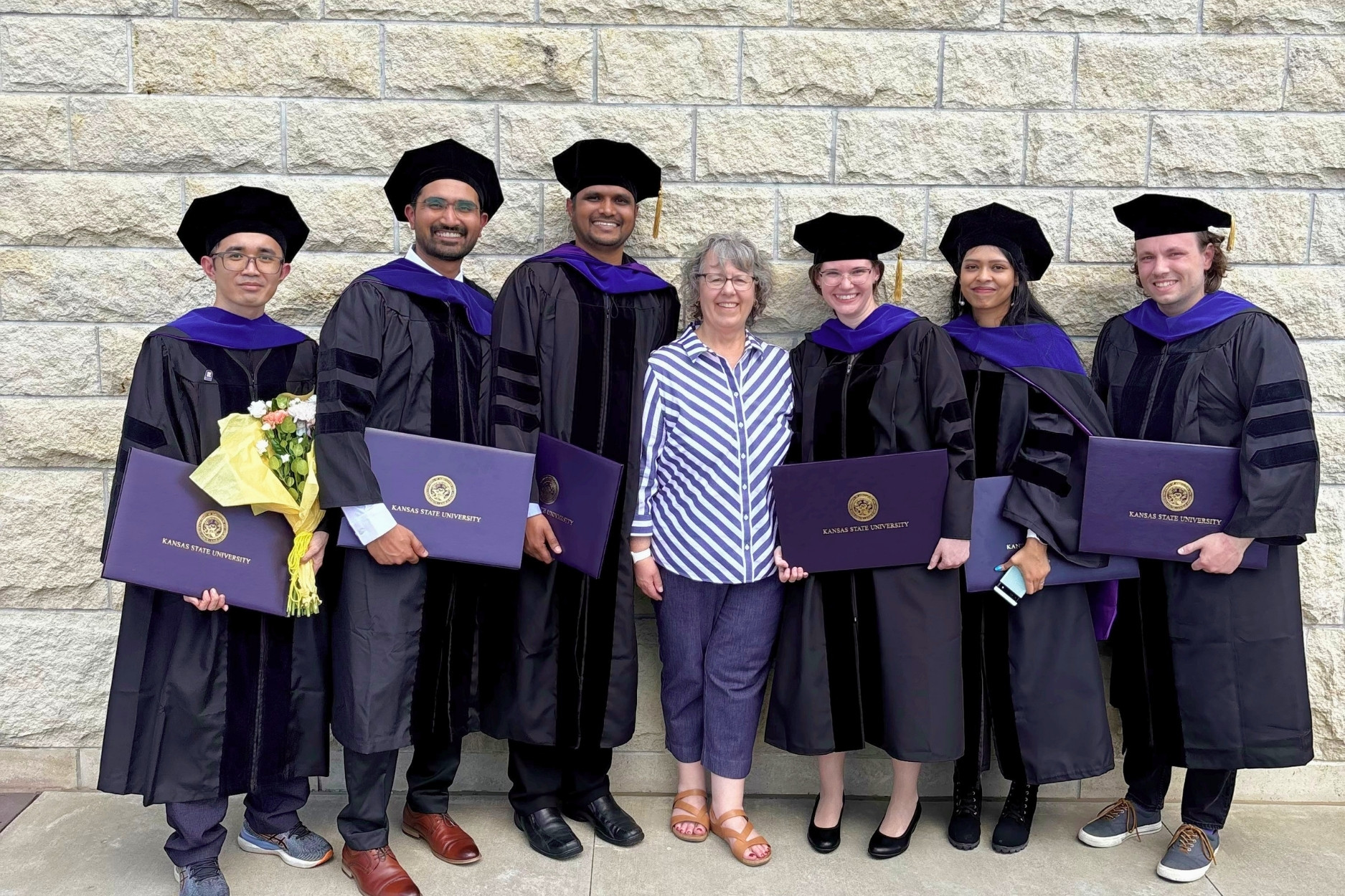 Kim Coy stands in the center of six doctoral graduates, three males on the left and three females on the right.