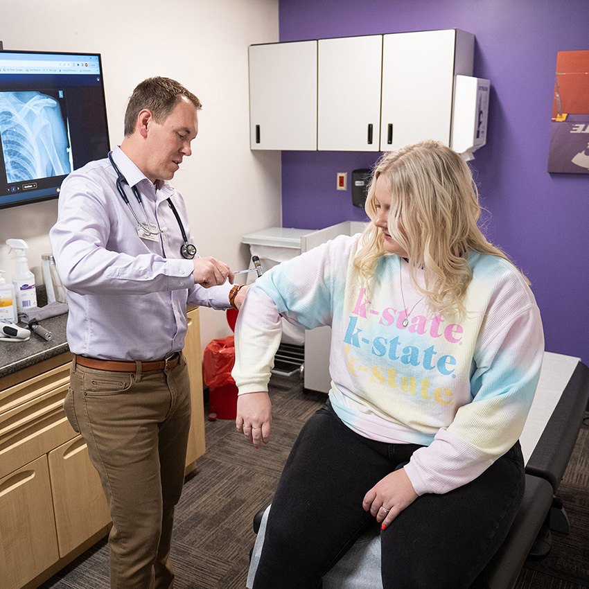 A healthcare provider takes the blood pressure of a college student in an exam room. 