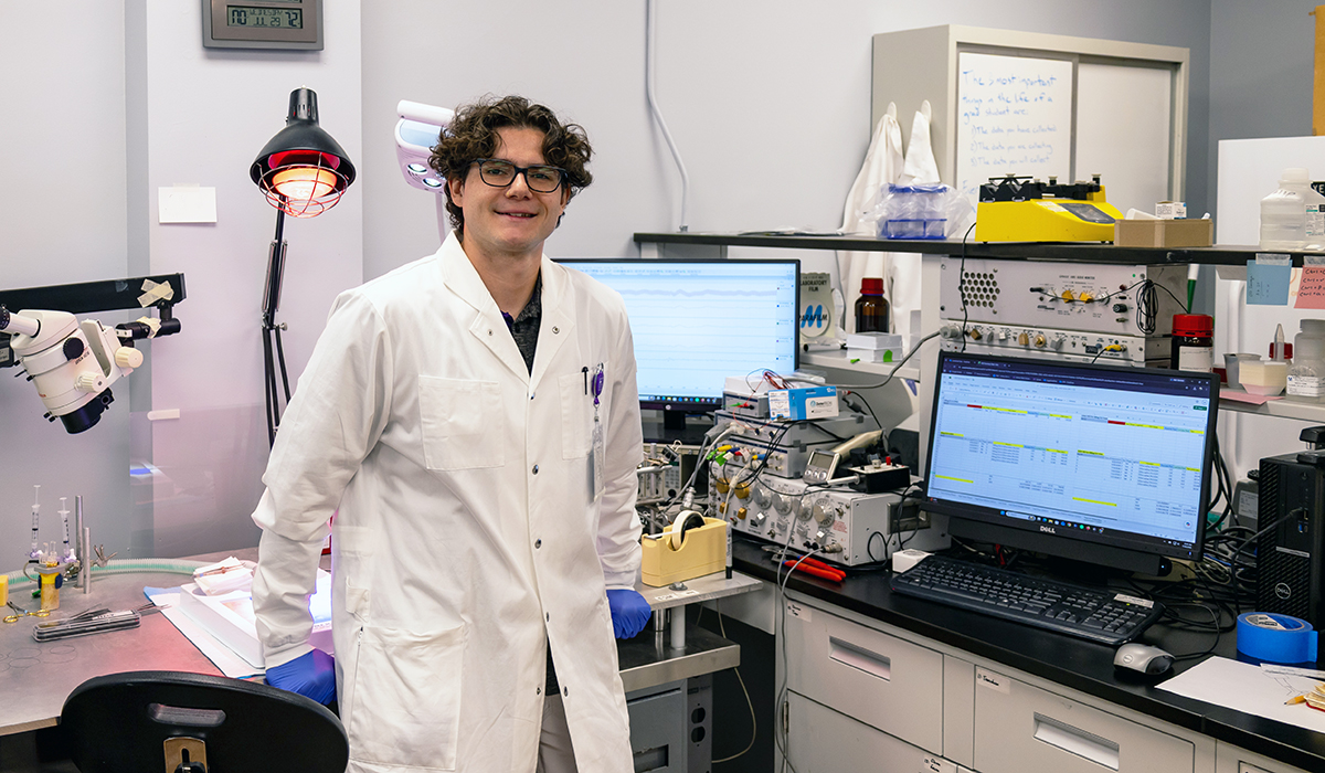 A male doctoral researcher poses for a portrait in front of his research work station.