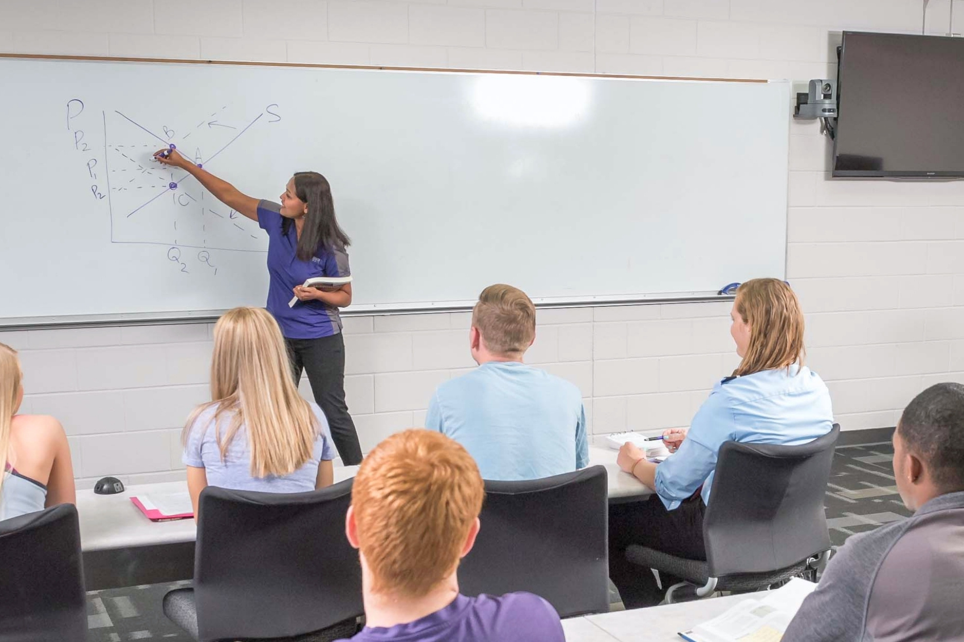 Siny Joseph writes on a whiteboard showing an equation while teaching a class.