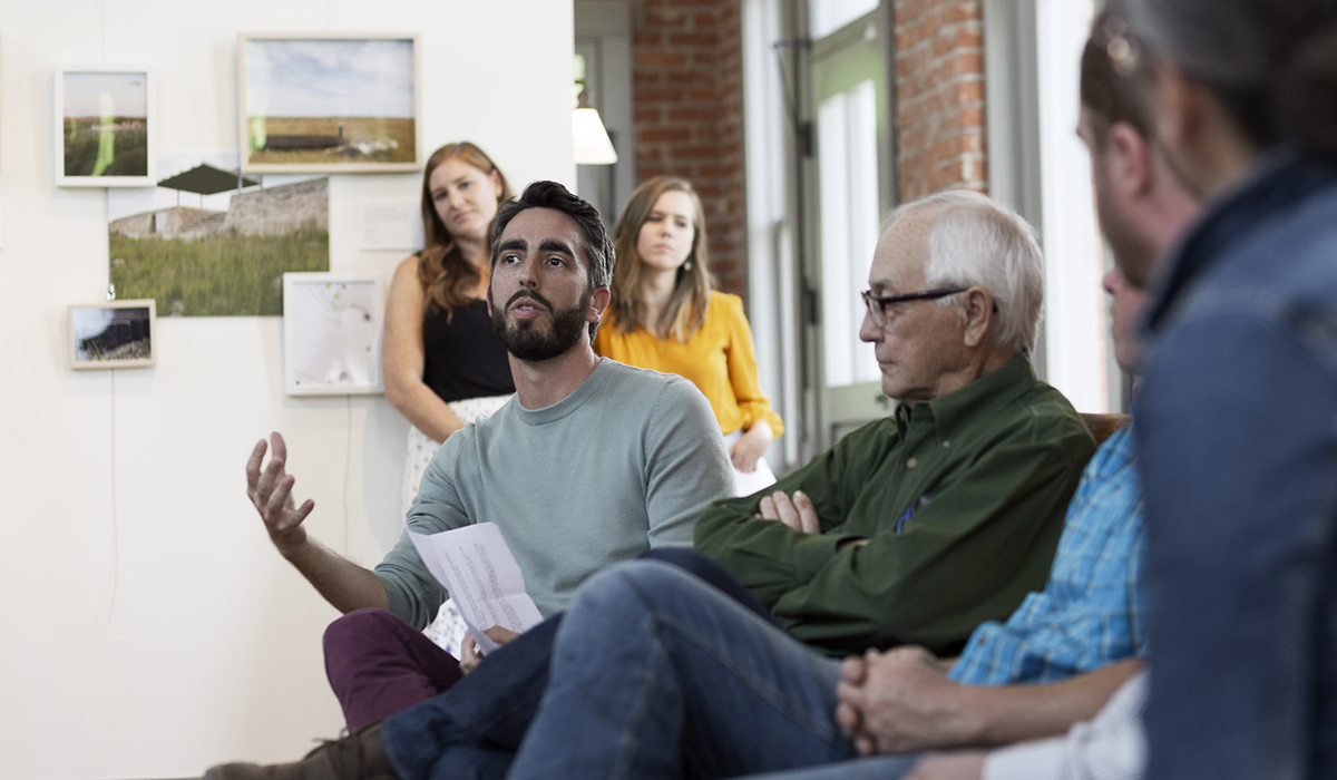 A man sits and presents on a panel in a college classroom.