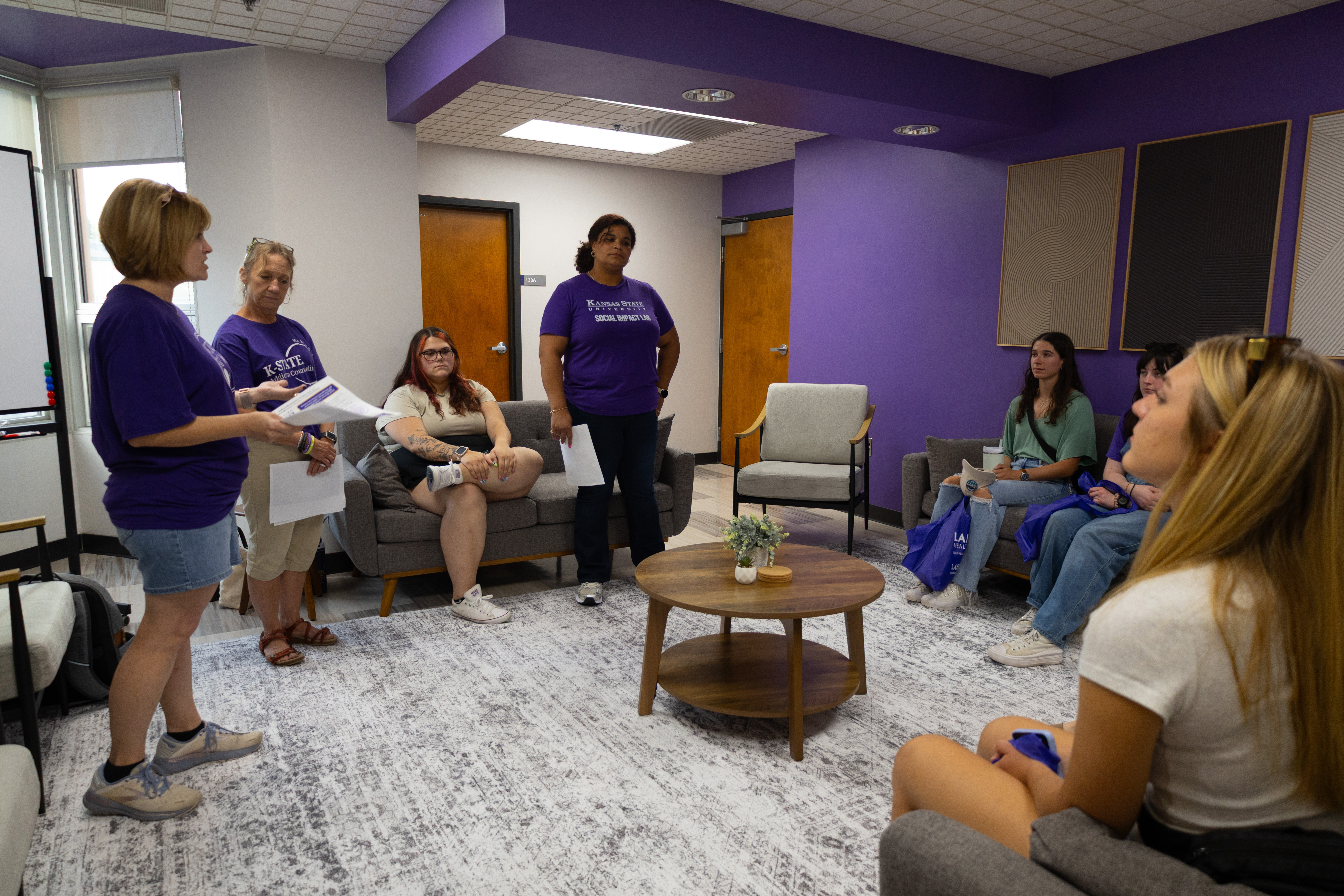 A group of college students and university staff members gather together in a campus meeting room to have a discussion. 