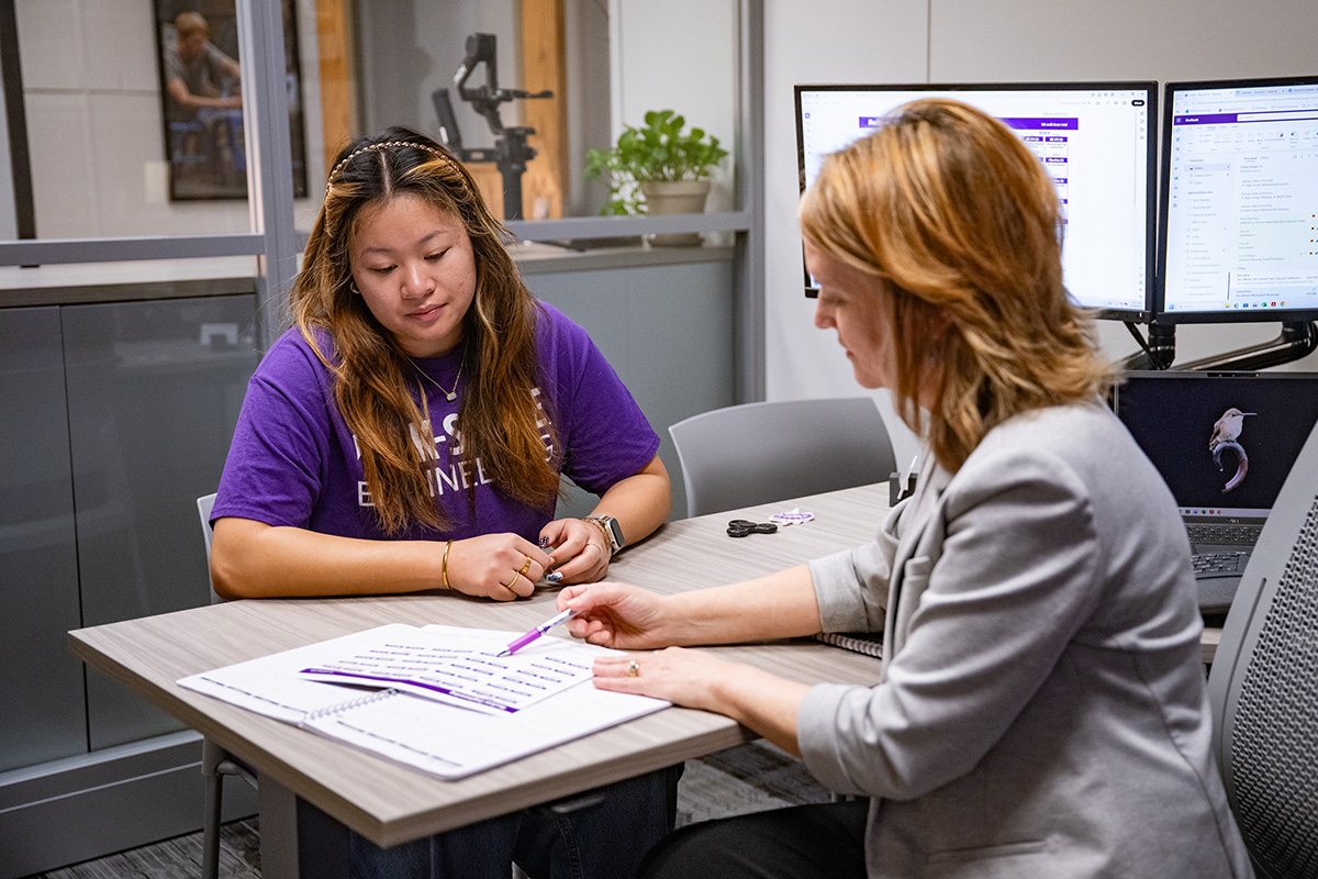 An academic advisor sits with a college student at a desk in an office.