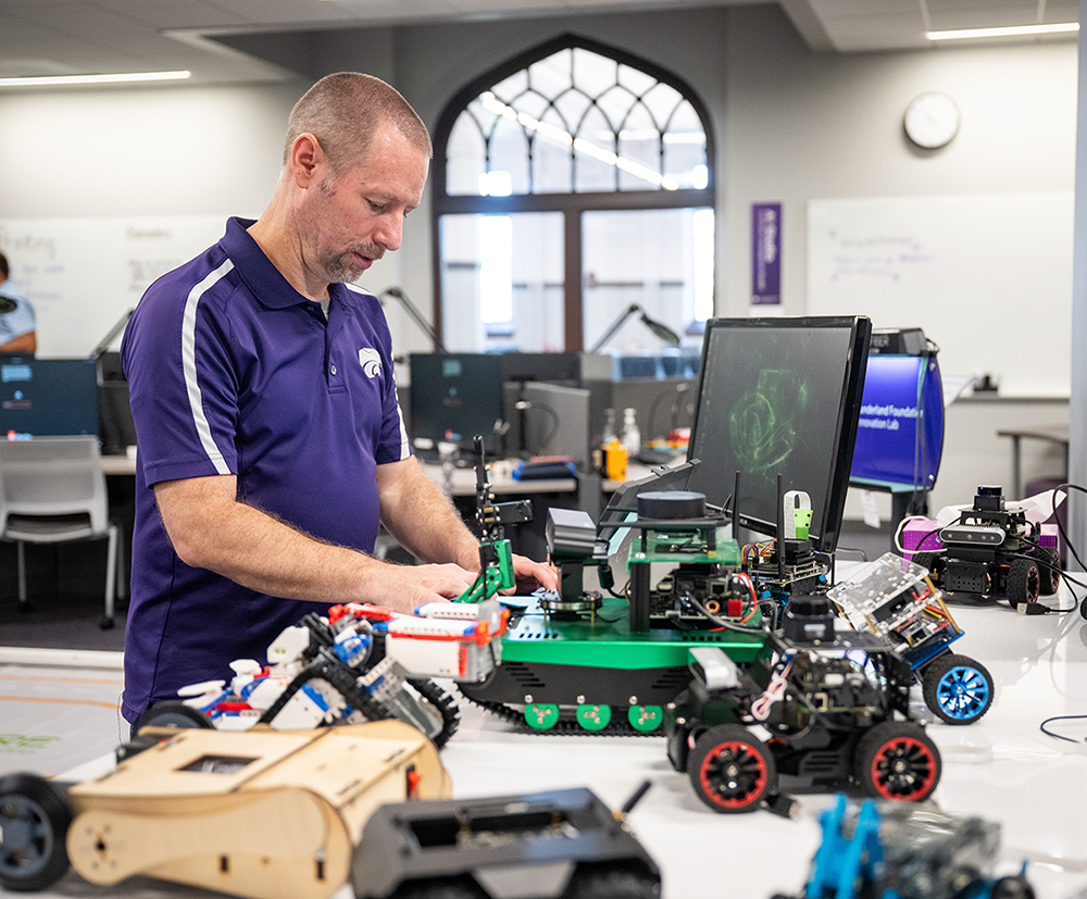 A man stands at a table with many robotic creations on it