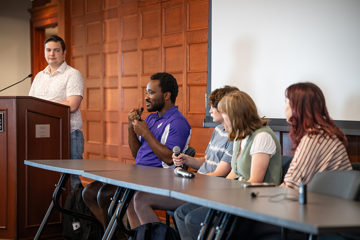 A student in a purple polo holds a lapel mic and speaks as part of a student panel.