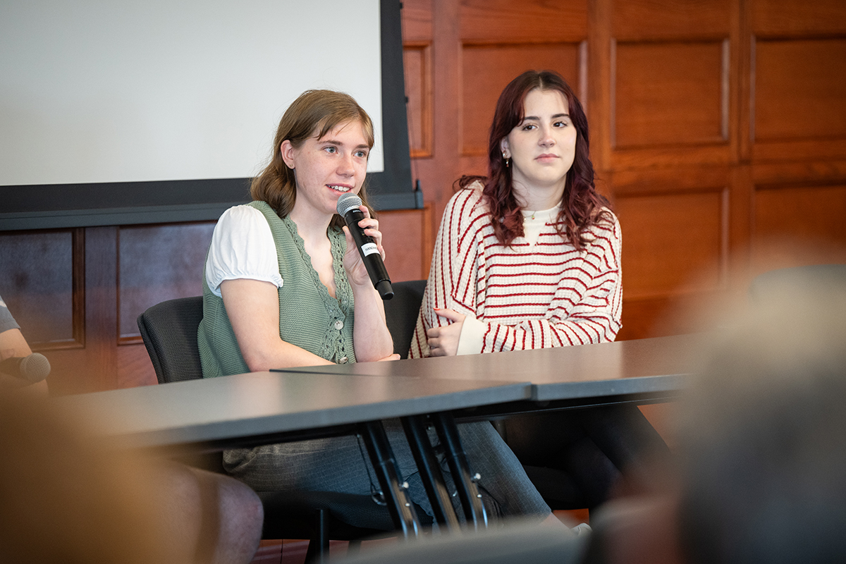 Two students are shown as part of a student panel; one holds a microphone.