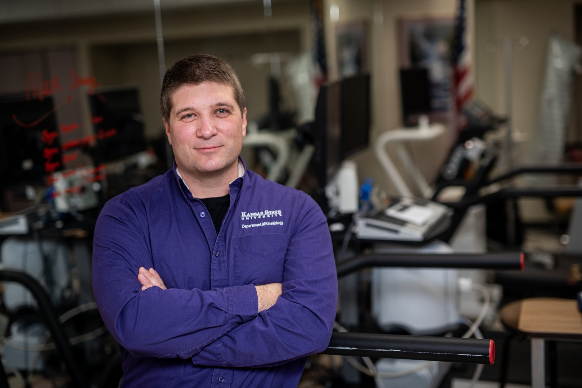Carl Ade poses for a photo in his lab, wearing a purple long-sleeved button-up shirt.