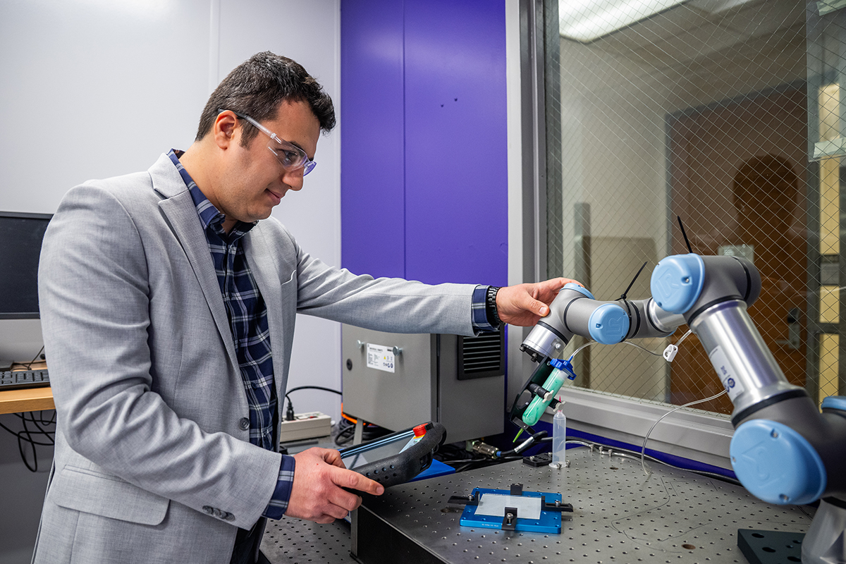 A professor in a suit works with a robotic arm and a handheld device in a lab