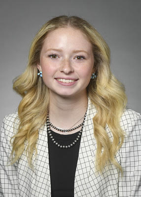 A young woman in a white checkered blazer is pictured against a gray background.