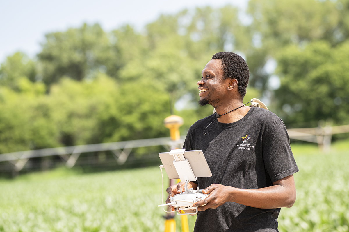 A doctoral researcher stands in a field and holds a drone controller.