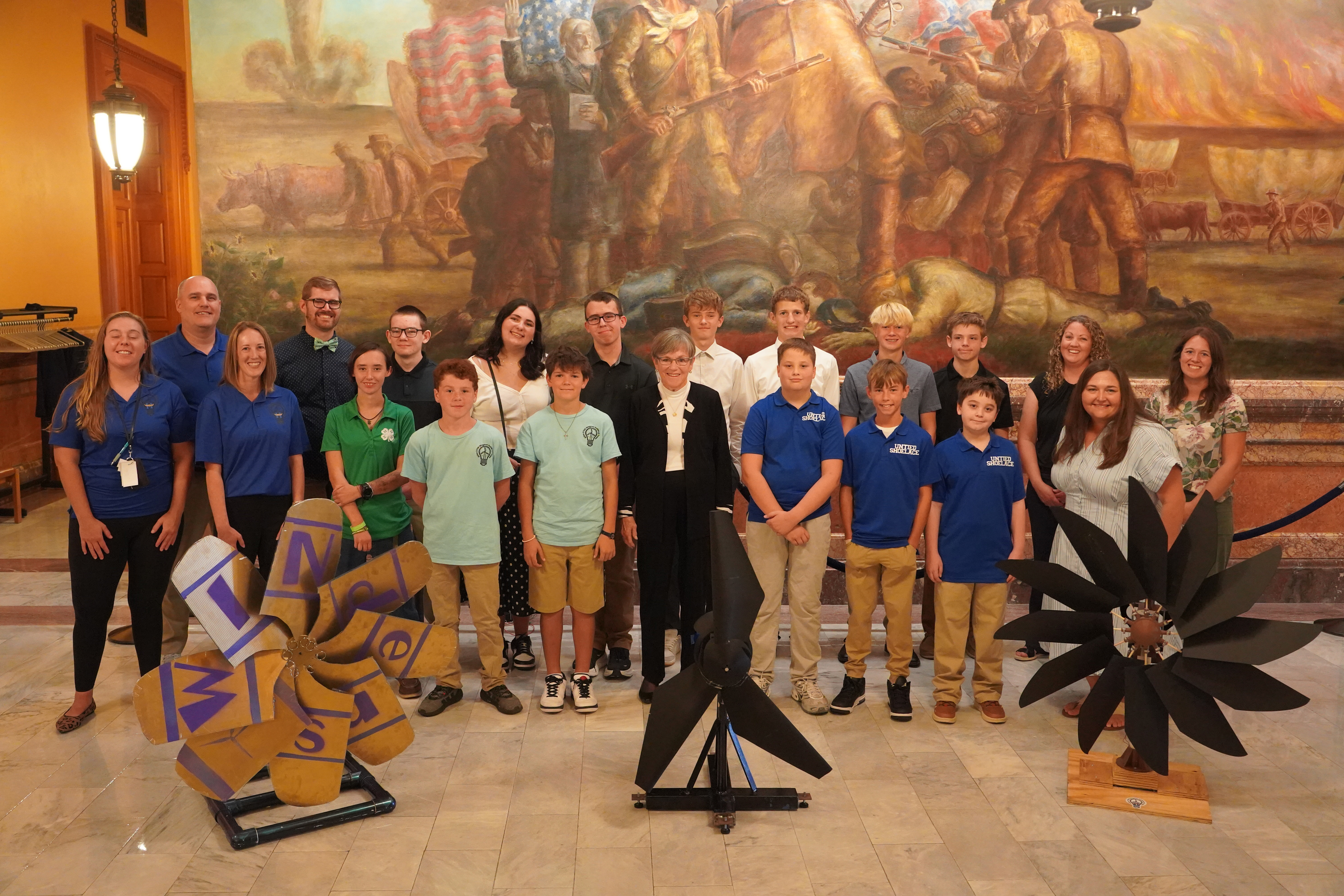 A group of K-12 students stands with Kansas Governor Laura Kelly in the Kansas State Capitol alongside their winning wind turbine designs. 