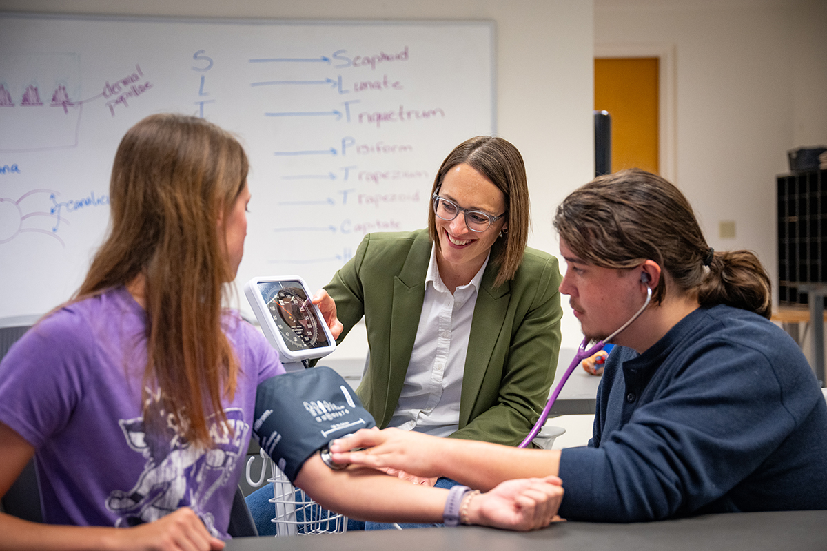 A woman instructs two students on taking blood pressure.