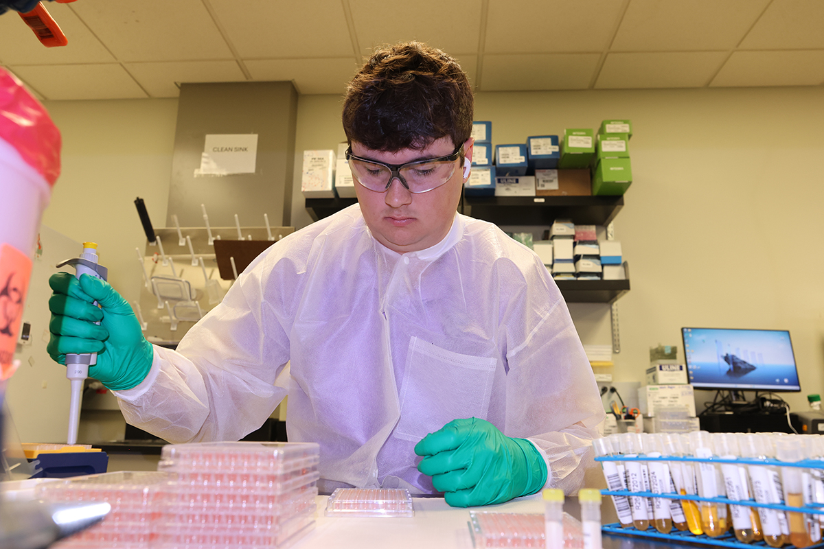 A laboratory worker uses a pipette to process some fluid for testing.