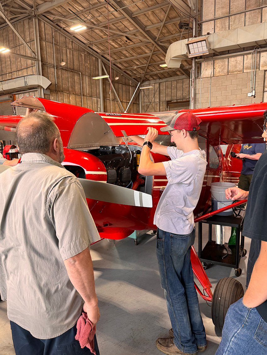 A student looks at the engine of a red plane.
