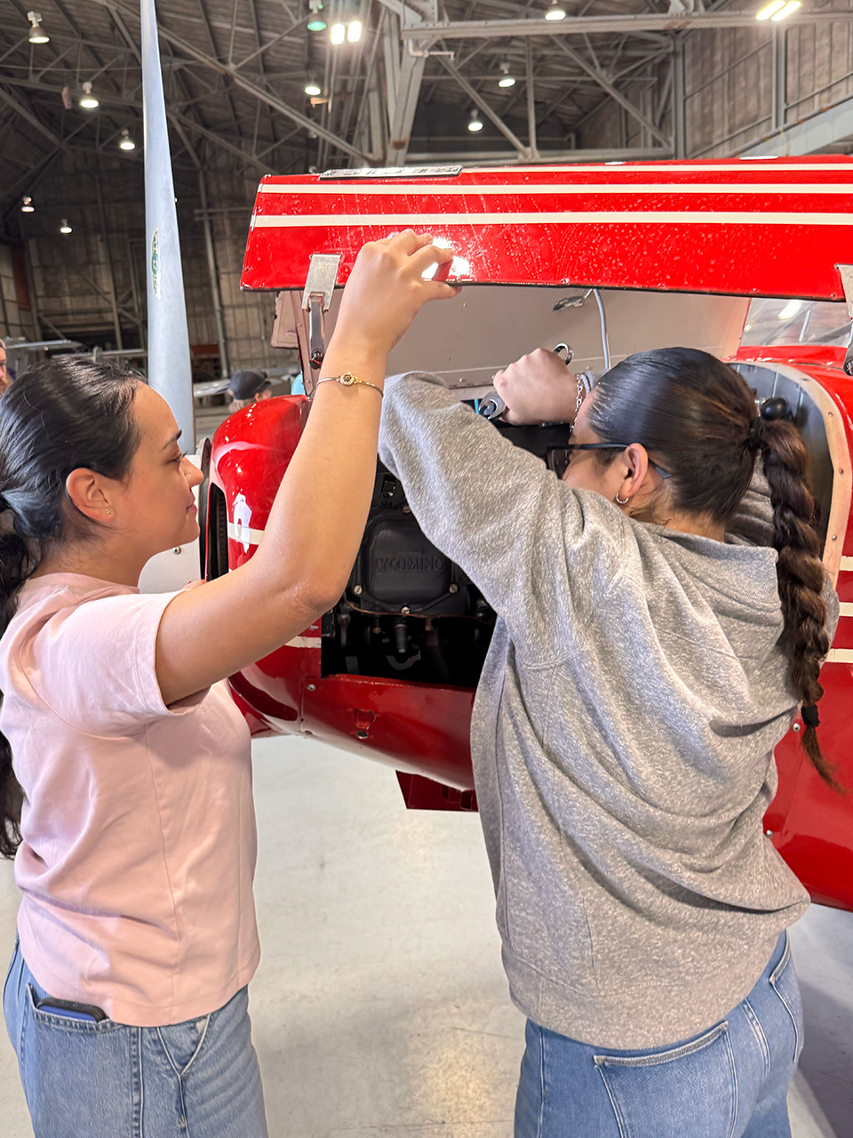 Two female students work on the engine of a red plane.