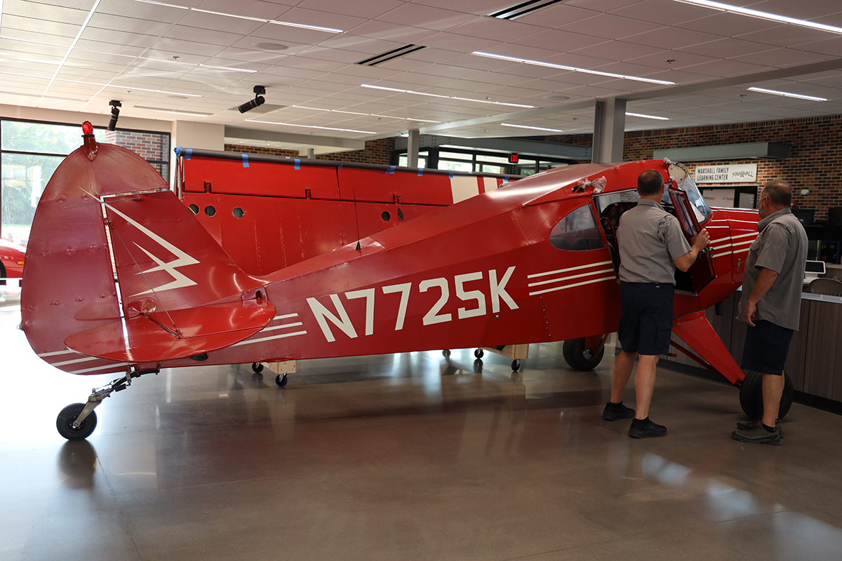 Two men look at the interior of a red plane.