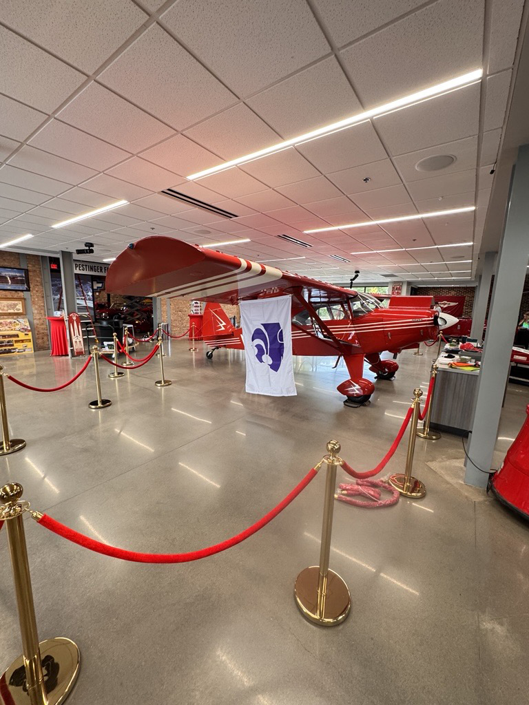 A red plane is displayed in a museum with a white banner showing a purple Powercat on it.