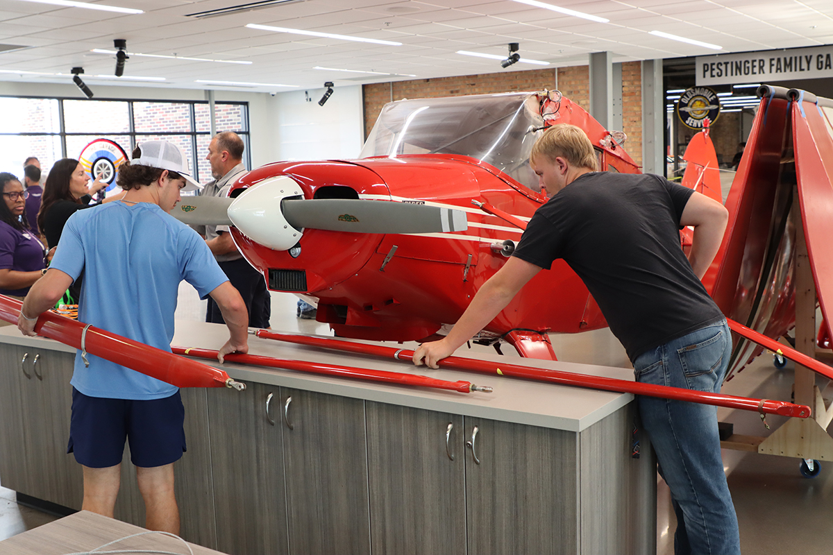 Two students handle red plane parts as they reassemble a plane in a museum.