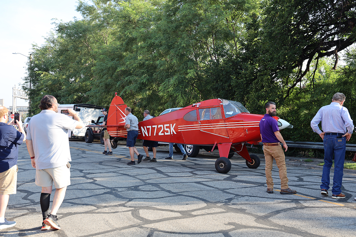 A red plane is pictured on a street with people taking photos of it.