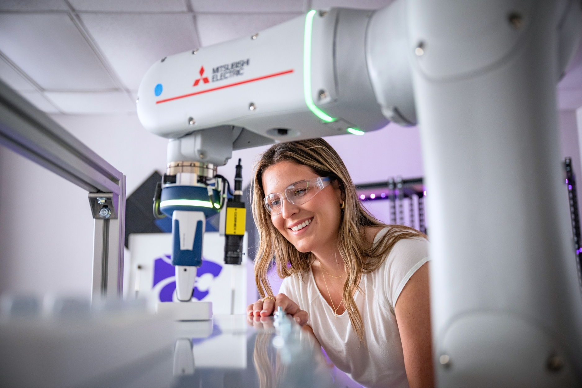 A student wearing safety glasses works alongside a robotic arm in a K-State Salina laboratory.