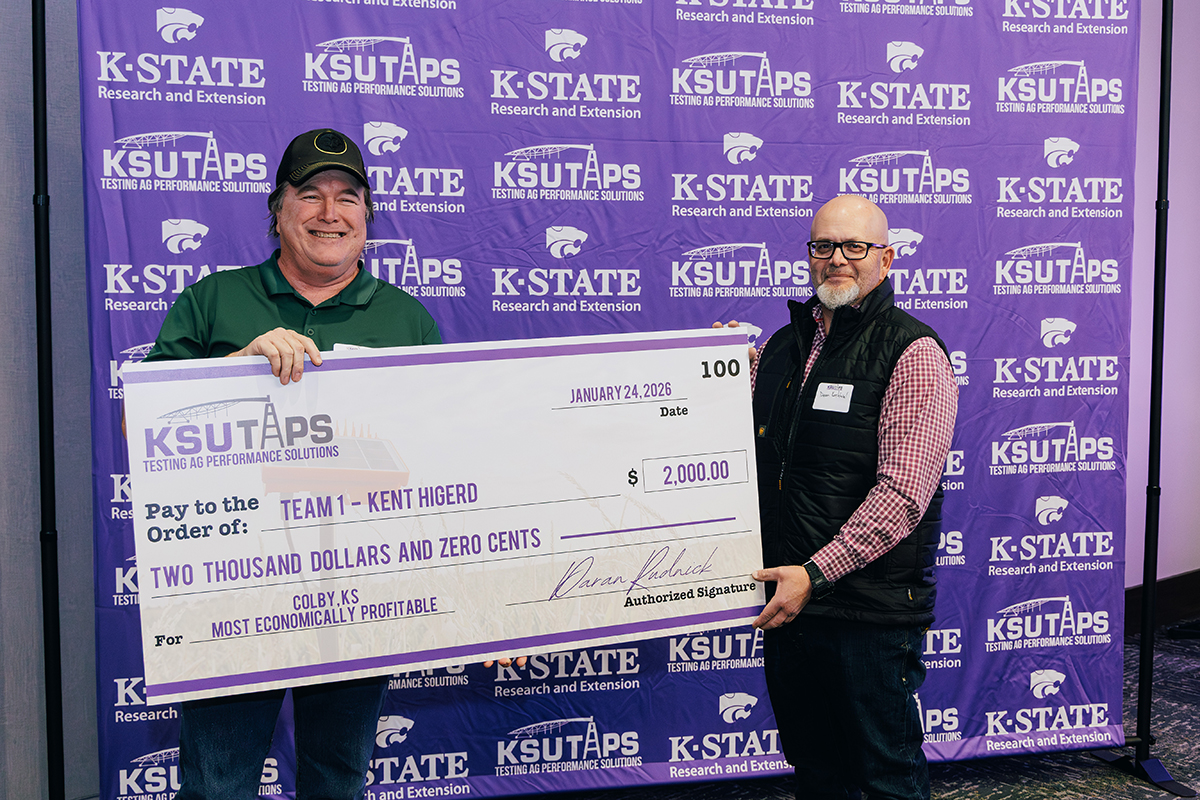 A farmer receives a check from a state official in front of a purple background.