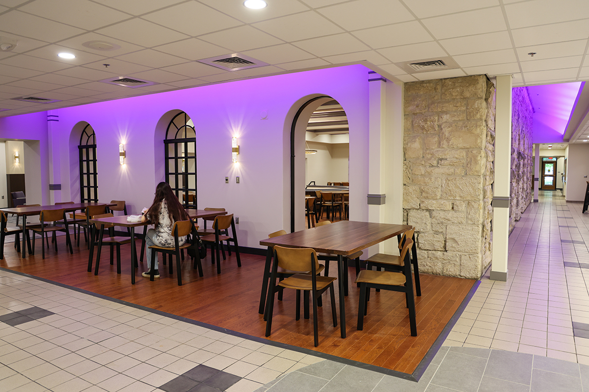 A dining center with three archways illuminated in purple is shown with sets of tables and chairs