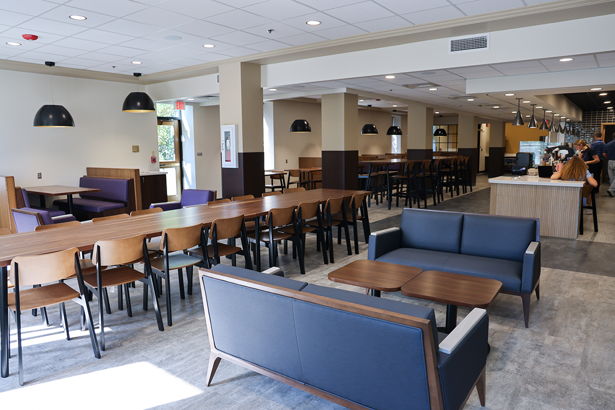 A seating area is shown in a campus dining center, including booths, couches with tables, and long tables surrounded by chairs.