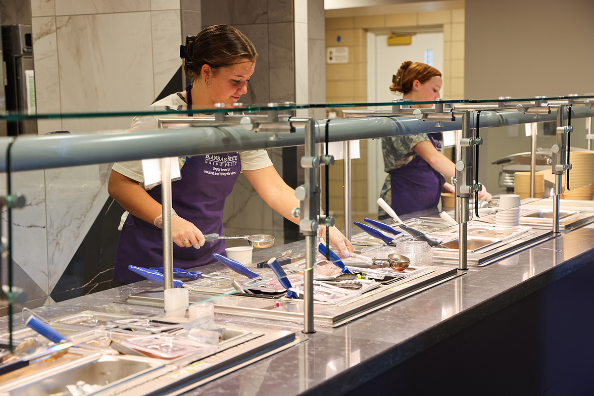 Two students serve meals in a campus dining center.