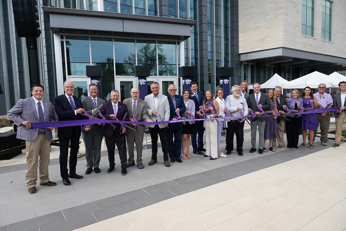 A group of people stand in front of a new building with large scissors to cut the ceremonial ribbon
