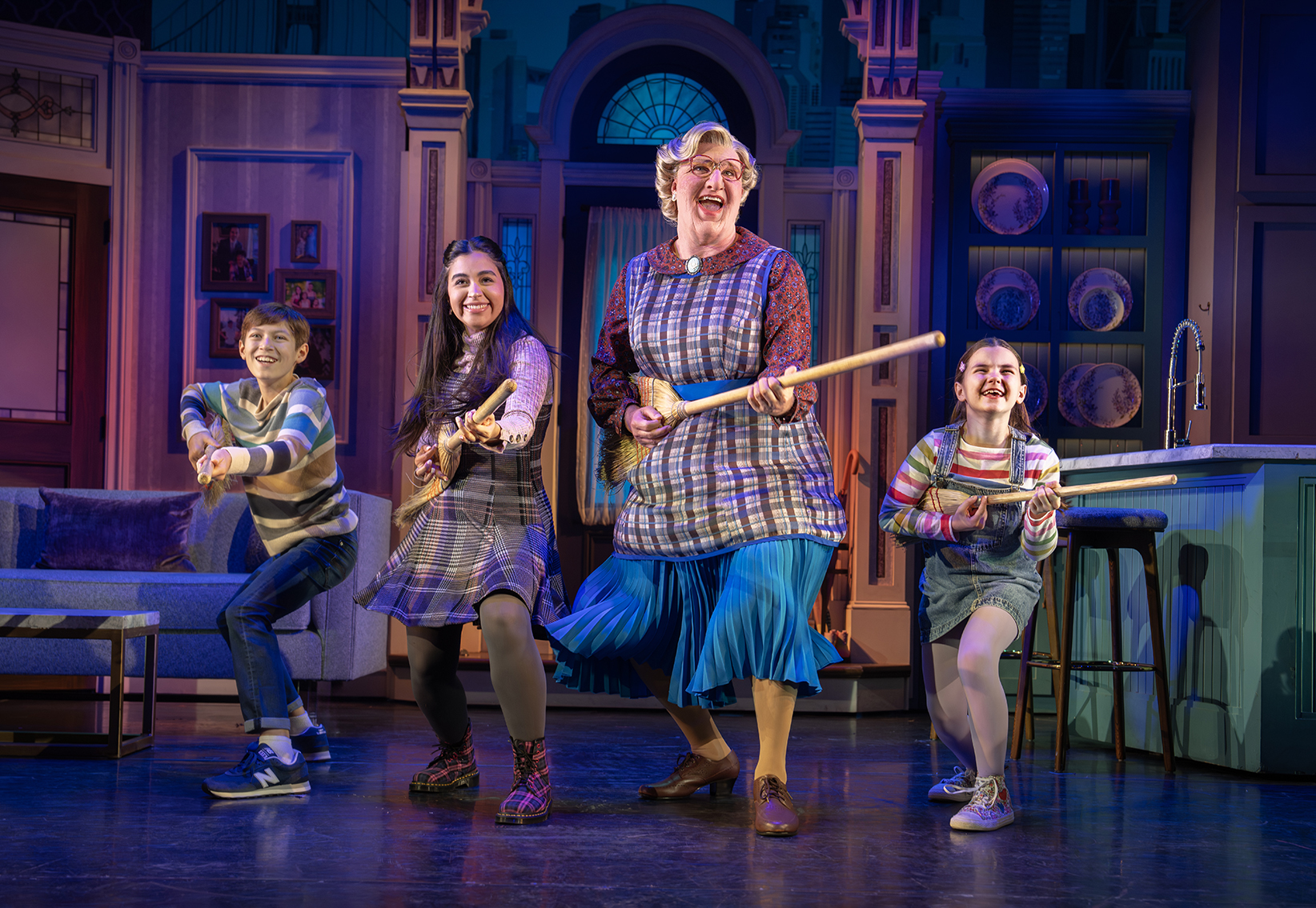 Three kids and an adult stand onstage holding brooms like guitars for a performance of Mrs. Doubtfire