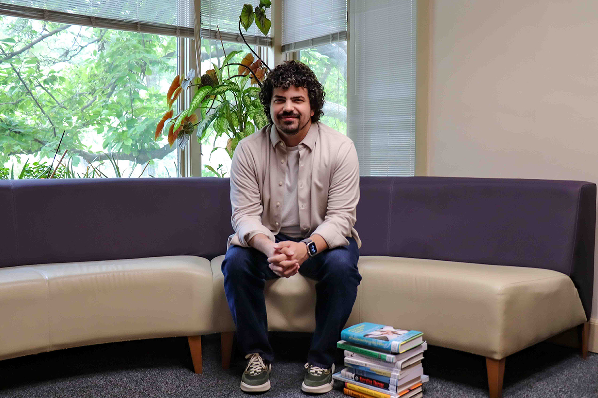 A male graduate students sits on a couch and poses for a portrait.