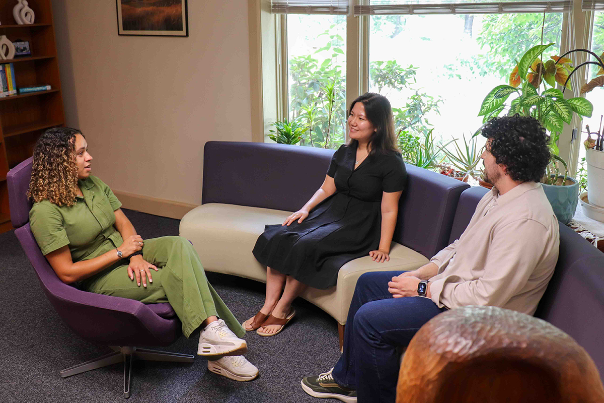 Three graduate students sit and hold a conversation.
