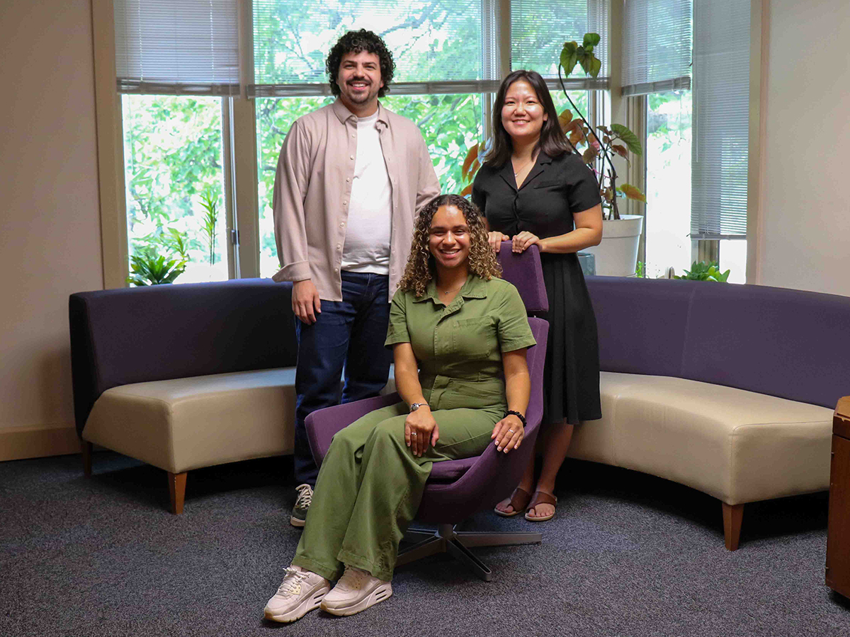 Three graduate researchers pose for a portrait in a small cozy office.