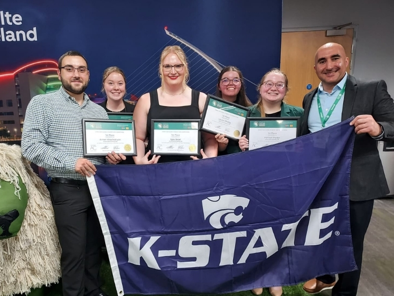 Aleksan Shanoyan stands with five students, holding a K-State flag and commemorative certificates in Ireland.
