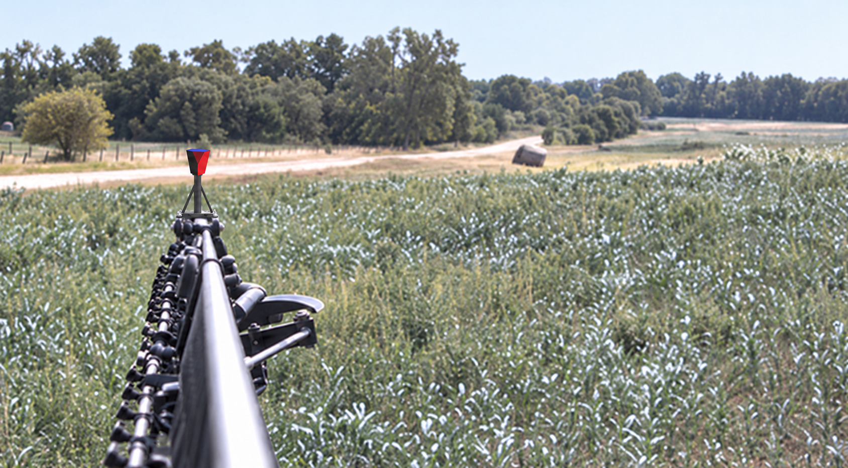 A red prismatic rectangle stands on the tip of a crop sprayer's boom over a field.