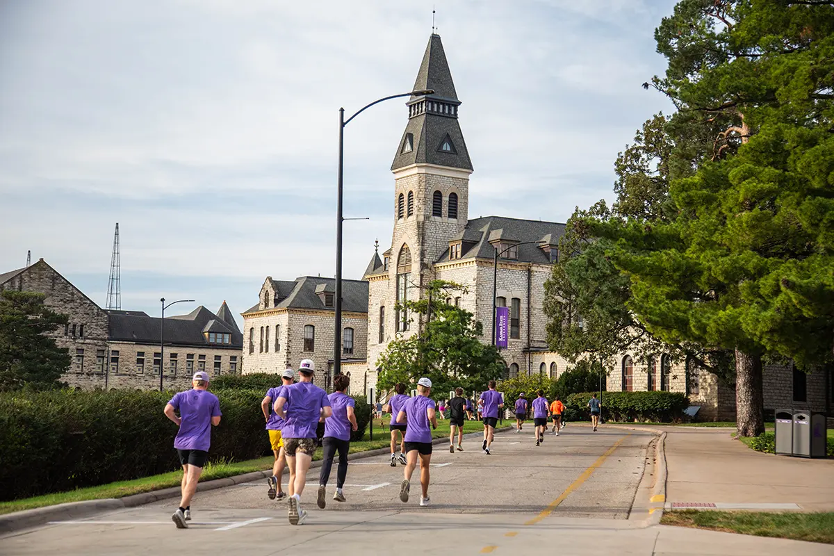 Groups of individuals run in front of a limestone academic building.