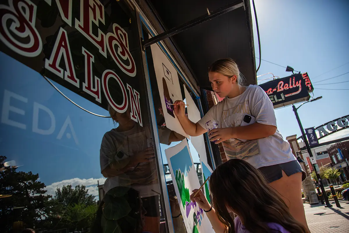 Two female students painting on a local business window.