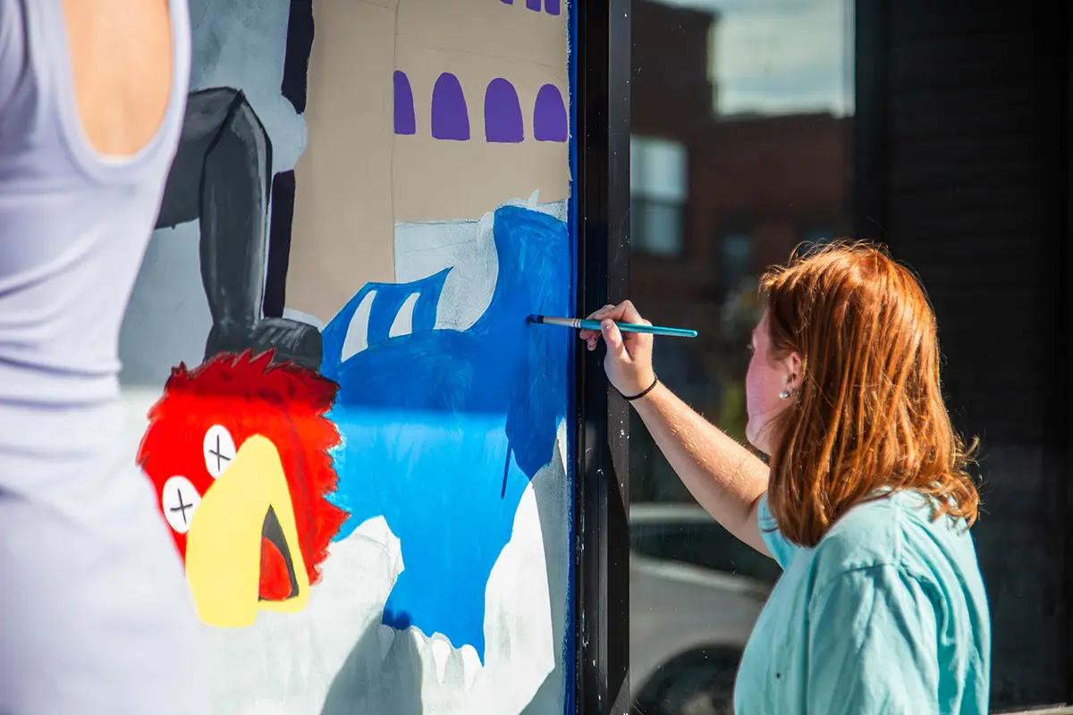 A female student finishing painting of KU Jayhawk with X’s in his eyes.