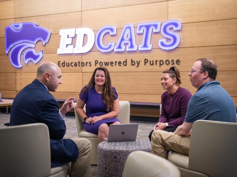 Jessica Lane sits with colleagues in the Bluemont Hall lobby talking.