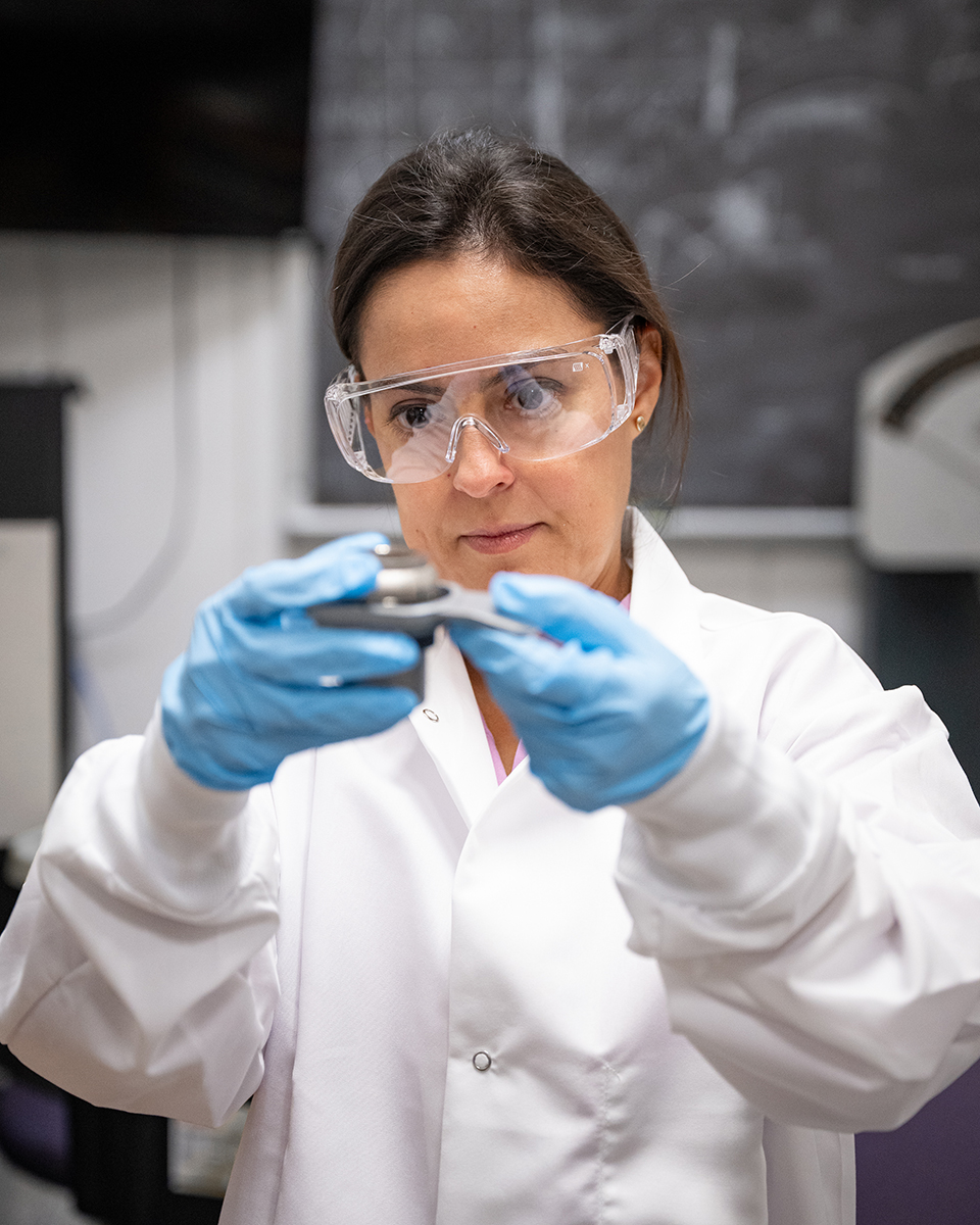 A woman in a white lab coat examines something she's holding up in front of her