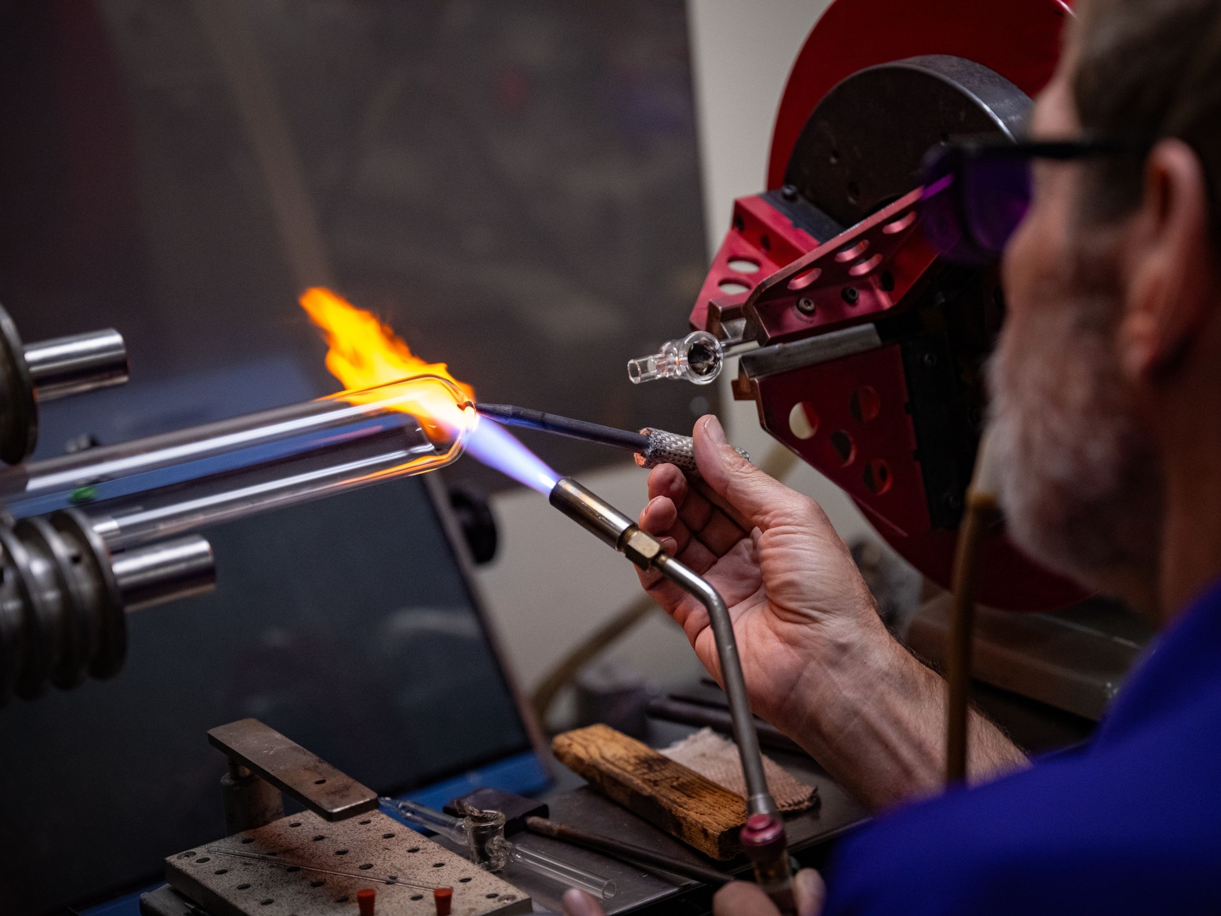Jim Hodgson uses a blowtorch at the glassblowing lathe to shape a borosilicate tube.