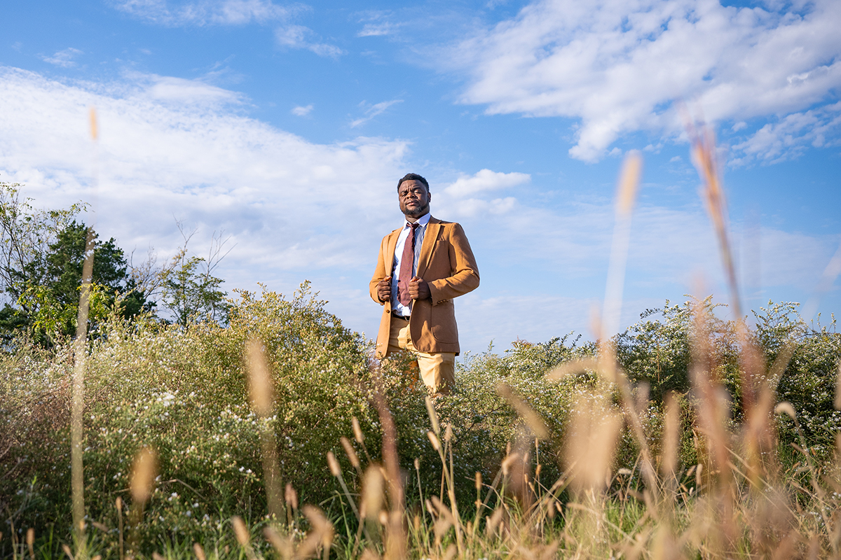 A researcher in a brown sportcoat stands in the middle of a grassy prairie.