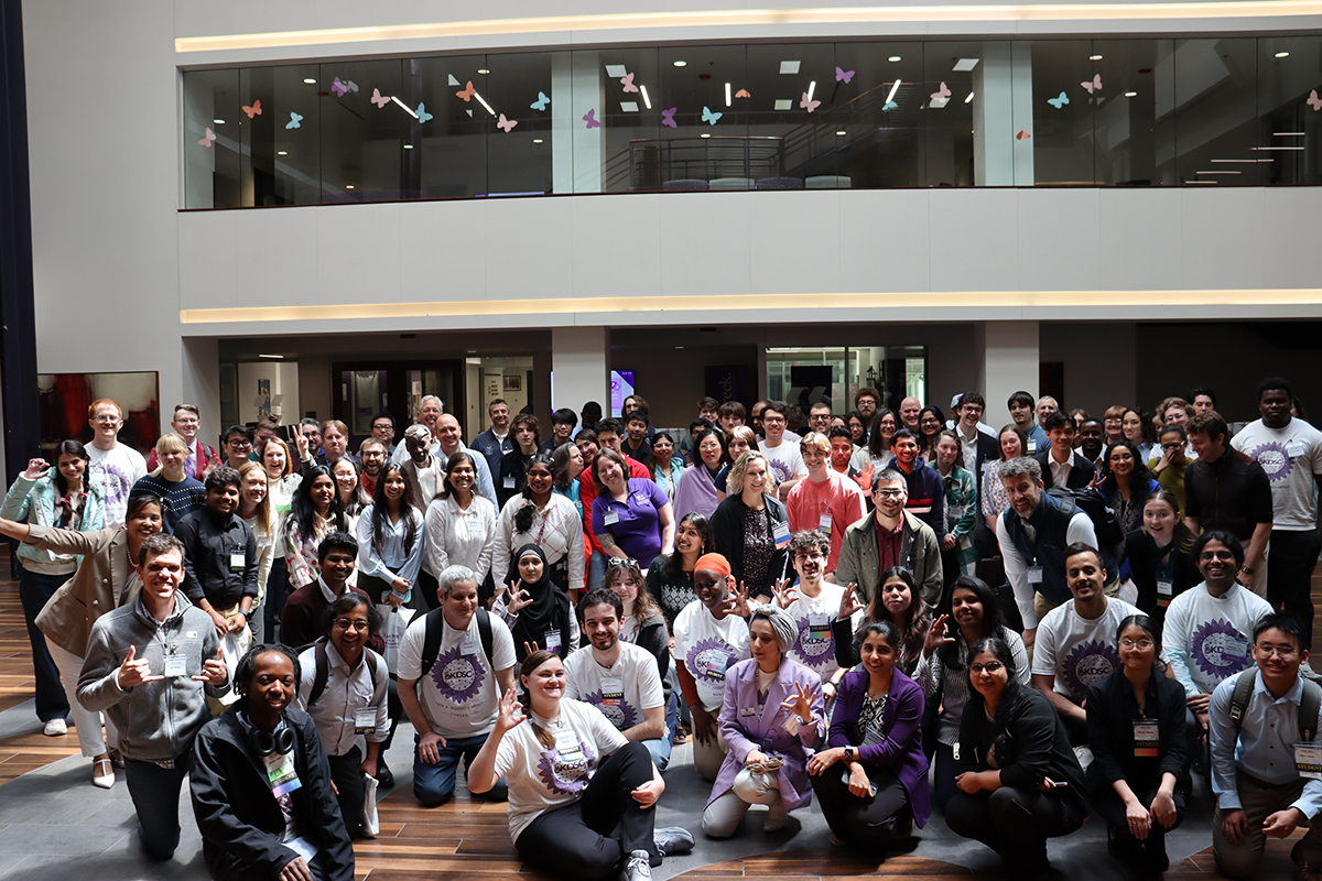 Several conference attendees pose for a large group portrait in a courtyard.