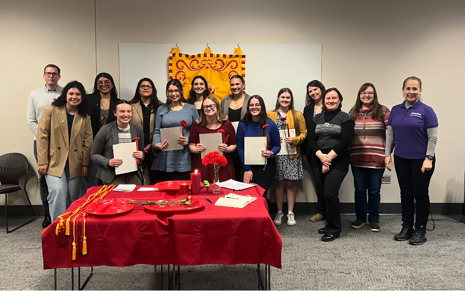 Students standing with certificates behind a red table that is set with candles.